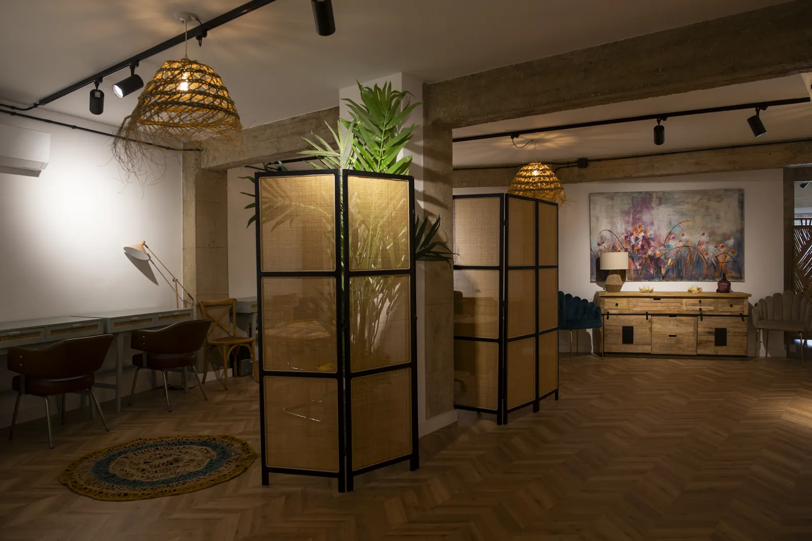 Sala del Centro de Día con biombos de madera y plantas, lámparas de ratán y un cuadro de colores al fondo