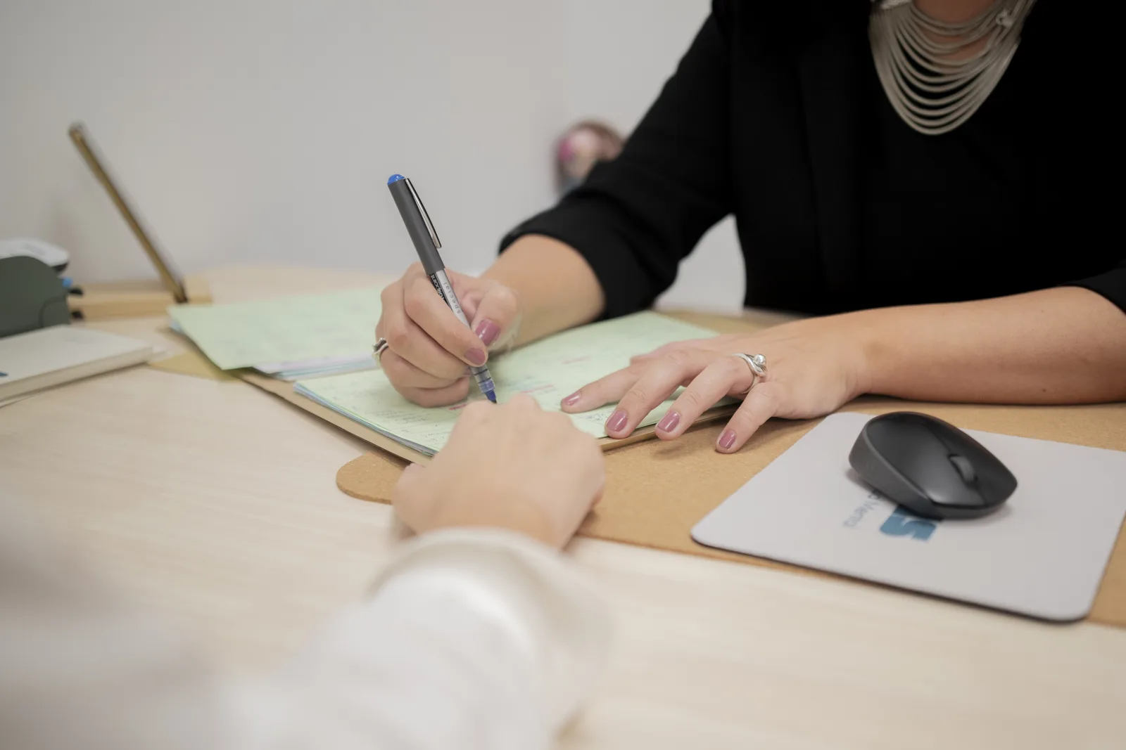 Manos de una profesional de Clínica Unitas rellenando un formulario en papel junto a una persona, sobre una mesa de despacho