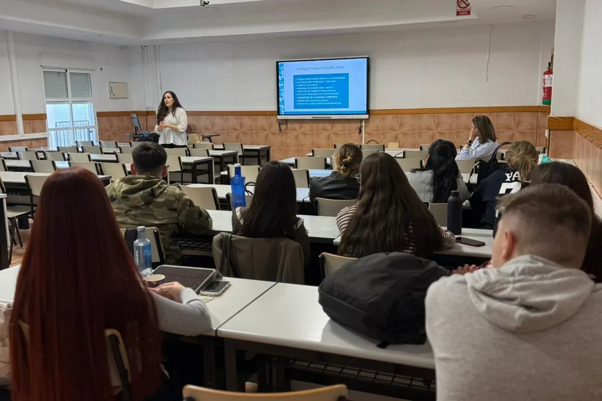 Charla de Clínica Unitas en un aula amplia: la ponente presenta junto a una pantalla con la diapositiva «Atención multidisciplinar» mientras el alumnado, de espaldas, la escucha